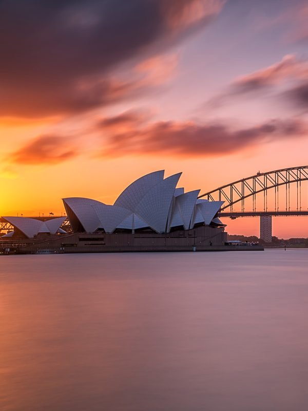 A beautiful shot of the Sydney harbor bridge with a light pink and blue sky in the background at sunset